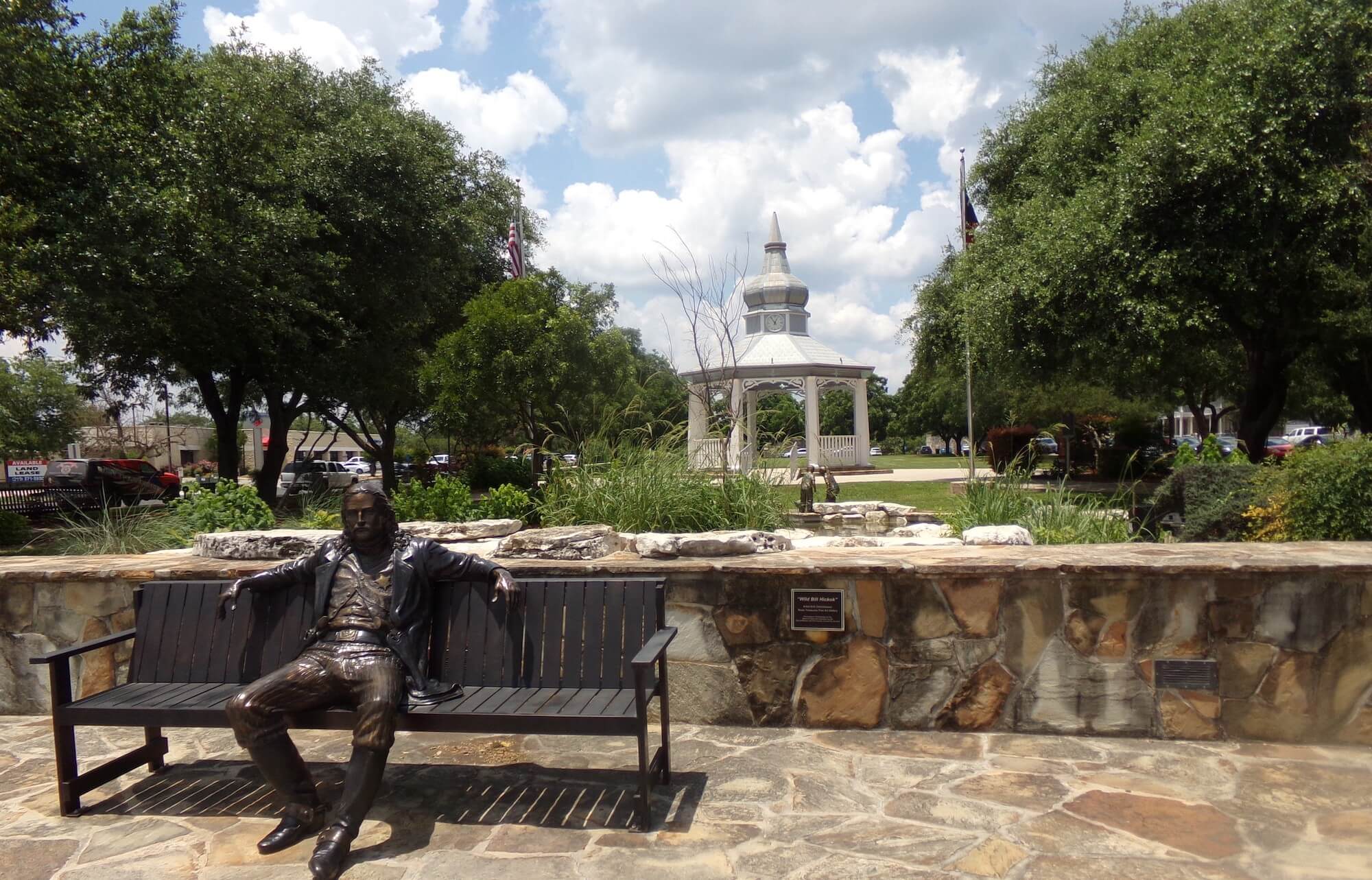 A statue of a man sitting on bench with a white gazebo in the background in Boerne, Texas.